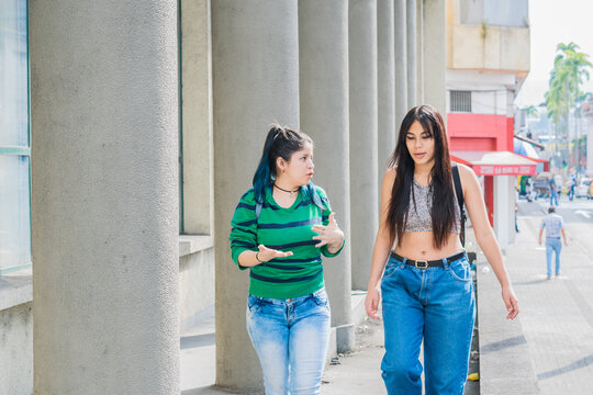 two beautiful latina girls (caucasian and brunette) walking down the street, talking about their studies and discussing their future. concept of education. explaining their thesis.