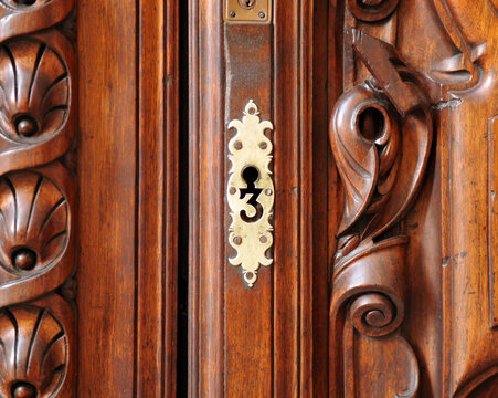 Ojo llave de latón con forma de 3 en una puerta de madera tallada con molduras. Ojo de cerradura de bronce en puerta antigua. Primer plano de cerradura