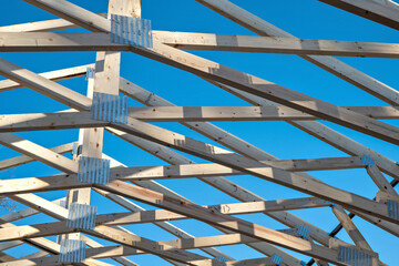 Roof trusses on a new home construction project with blue sky in the background. Wood house structure with graphic pattern on blue background.