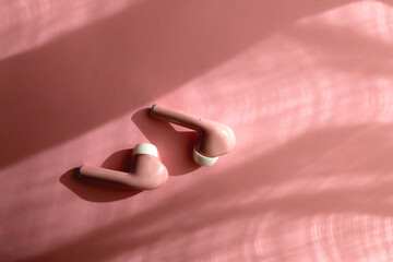 Pink wireless bluetooth earphones on pink background. Flat lay.