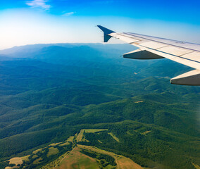 View of airplane wing, blue skies and green land during landing. Airplane window view.