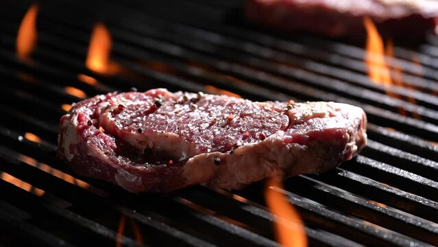 Raw seansoned steak meat beef dropped on flaming grill. slow motion