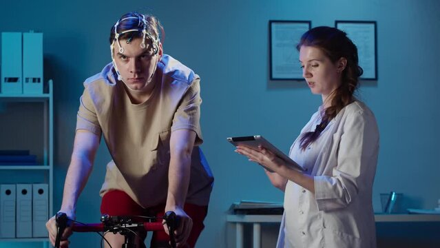 EEG topographer for examining brain, doctor making electrogram of scalp activity. Researching of brain work, man riding bicycle in electroencephalography headset. Rehabilitation after damage in sport.