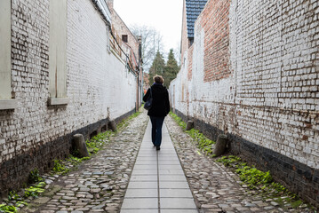 Fototapeta na wymiar Woman walking through a small alley with a paved road an old bricked walls at the beguinage of Dendermonde, Flanders, Belgium