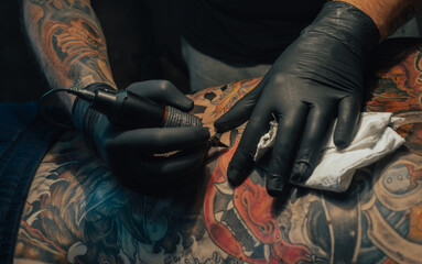 Hands of a tattoo artist holding a machine while working - obrazy, fototapety, plakaty