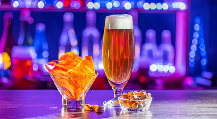 Glass of beer on bar counter. Jugs, mugs, pints of brew beverage, ale, cider on wooden table in pub, bar. Backlit dark showcase with craft beer bottles in brewery. French fries fried potatoes snack