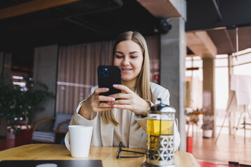 Young beautiful woman businessman uses smartphone for business, online shopping, money transfer, finance, internet banking. Woman working in a cafe