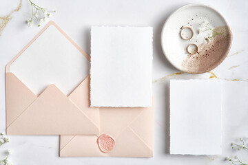 Elegant wedding stationery top view. Flat lay blank paper card, pink envelopes, golden rings on...