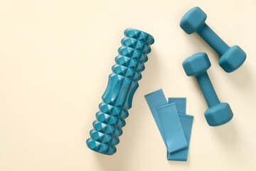 Blue workout equipment set on beige background. Dumbbells, fitness tape, roller. Flat lay, top view.