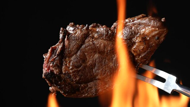 Cooked juicy steak meat beef on a metal roasting fork with flames in the background. slow motion