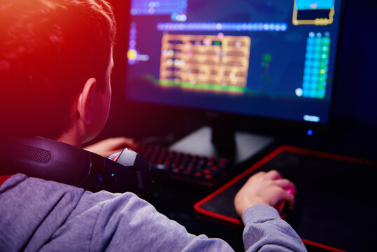 Teenager boy play computer video game in dark room, use neon colored rgb mechanical keyboard, workplace for cybersport gaming, children gaming addiction