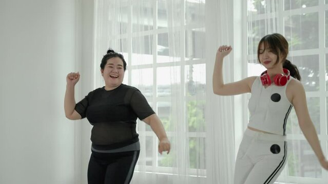 beautiful Asian woman and fat woman practicing dancing in the room cheerful and happy. Concept of exercise and body weight loss
