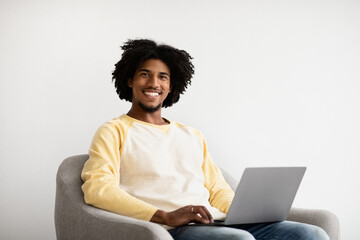 Remote Career. Smiling Black Guy With Laptop Sitting In Armchair At Home