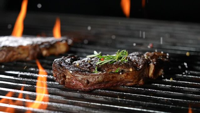 Cooked juicy steak meat beef sprinkled with seasoning on a flaming grill. slow motion