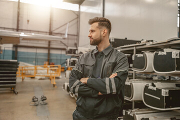 Fototapeta na wymiar Male aviation maintenance technician keeping arms crossed and looking away while standing in aircraft repair station