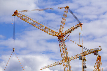 Yellow building tower cranes during their work on the background of a cloud blue sky. The concept of renovation and construction of modern buildings and structures.
