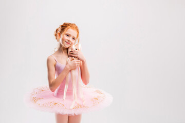 Portrait of a little tender red-haired girl in a pink tutu with pointe shoes, dreaming of becoming...