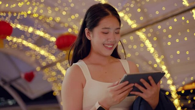 at night,young Asian woman happily plays with the tablet .She looks forward with hopes and dreams, a technology device of today in the middle of an urban society with buildings a in the backdrop.
