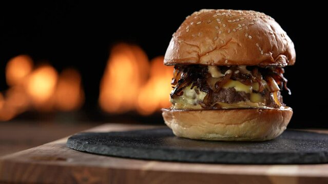 Meat cheeseburger with caramelized onion on black plate slide onto the frame with flaming background. slow motion
