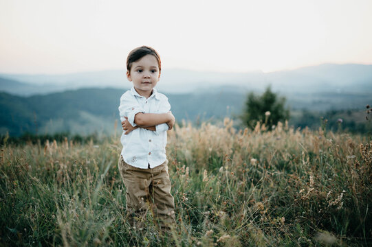 A child boy stands in a field of grass with hands around his waist