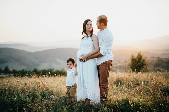 Pregnant woman holding his son and husband hands at sunset