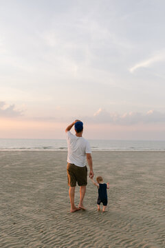 Dad holding toddler's hand on beach and walking towards sunset