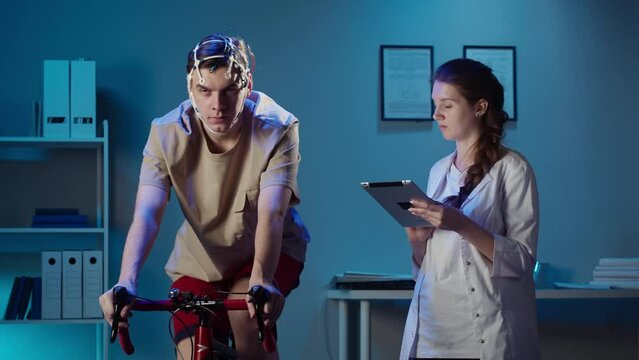 EEG topographer for examining brain, doctor making electrogram of scalp activity. Researching of brain work, man riding bicycle in electroencephalography headset. Rehabilitation after damage in sport.