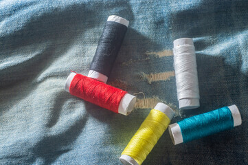 Reels with colorful sewing threads with jeans in the background, sewing concept, copy space in parts of the image