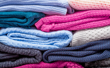 Knitted warm winter clothing folded in a pile. The surface of woolen things as a background. Closeup of knitted texture. Background with textile copy space. Casual wear.