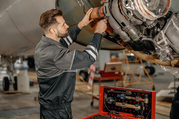 Bearded man maintenance technician tightening bolt with wrench while repairing airplane at repair...