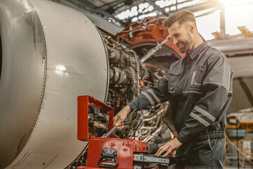 Smiling man maintenance technician grabbing wrench from instrument box while standing near airplane at repair station