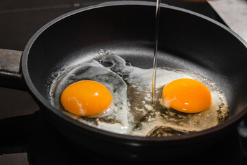 Two eggs on a hot non-stick surface of a metal frying pan for cooking scrambled eggs on an induction stove for breakfast