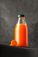 Juice of carrot in glass bottle. Freshly squeezed juice on dark background. Mock up for packaging and menu