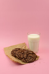 Glass of fresh milk and chocolate cookies on color pink background, copy space. Healthy food