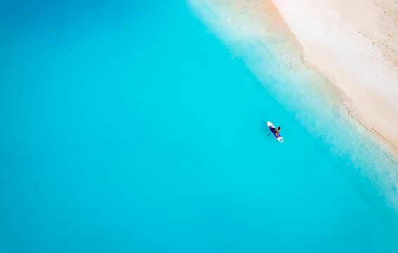 Aerial top down view of a woman on a stand up paddle (SUP) board over turquoise sea next to a tropical paradise beach in the Bahamas © moofushi