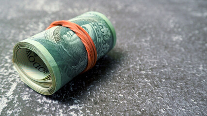 a bundle of Polish 100 zloty banknotes tied with a red rubber band lies on a gray background. side view. Polish money