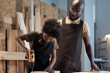 Portrait of cute African-American boy with father in workshop building wooden furniture, copy space