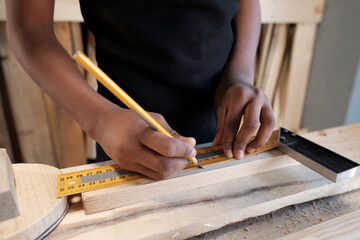 Close up of African-American boy measuring piece of wood in carpentry workshop, copy space - obrazy, fototapety, plakaty
