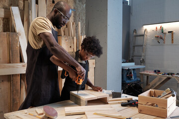 Portrait of African-American father and son bonding in workshop while building wooden furniture...