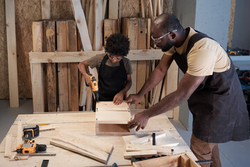 Portrait of African-American father and son bonding in workshop while building wooden birdhouse...