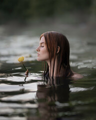 Red-haired girl in the water sniffing a yellow water lily