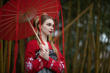 A girl in a national hanbok under a red umbrella among bamboo