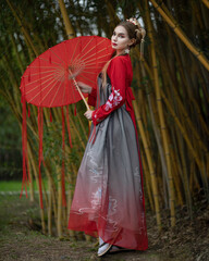 A girl in a national hanbok with a red umbrella with ribbons among yellow bamboo