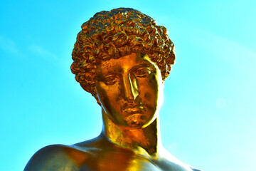 ancient golden statue of a man's faces close-up against the blue sky