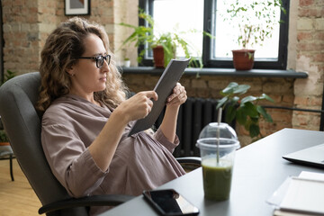 Pregnant businesswoman sitting on chair and reading documents in folder while sitting at the table with fresh cocktail