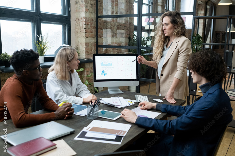 Aufkleber pregnant businesswoman pointing at computer monitor with financial graphs and talking to her colleag