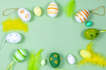 Easter frame with eggs and feathers on a green background. Minimal concept. View from above. Card with copy space for text.