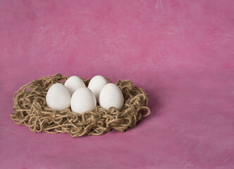 white eggs in a nest on a pink background. easter eggs. Copy space