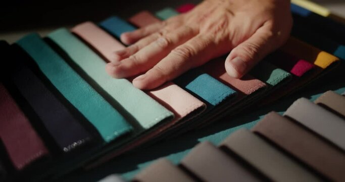 A man's hand touches samples of multi-colored fabric. Designer selects textiles for the project. Static shot