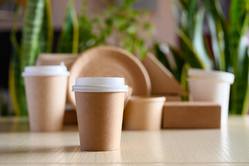 Paper disposable cup for coffee or tea on the background of eco-friendly dishes and green plants. The concept of protecting the planet from plastic.